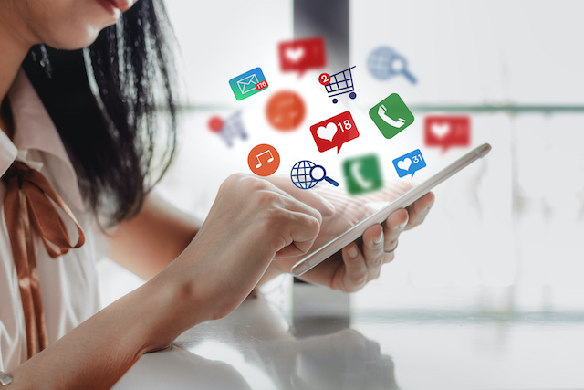 kobieta trzyma w dłoni smartfon, nad nim widnieją ikony social media